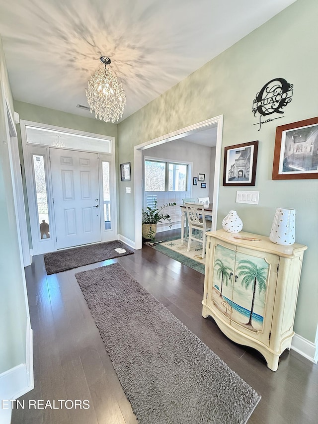 foyer with a notable chandelier, dark wood finished floors, visible vents, and baseboards