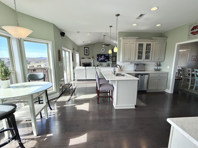 kitchen with lofted ceiling, a peninsula, light countertops, stainless steel dishwasher, and glass insert cabinets