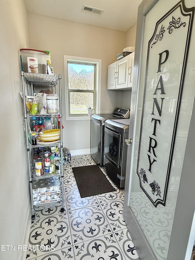 laundry area featuring washing machine and dryer, visible vents, baseboards, cabinet space, and tile patterned floors