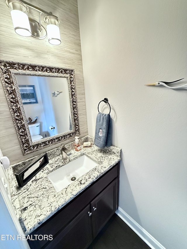 half bathroom featuring toilet, baseboards, and vanity