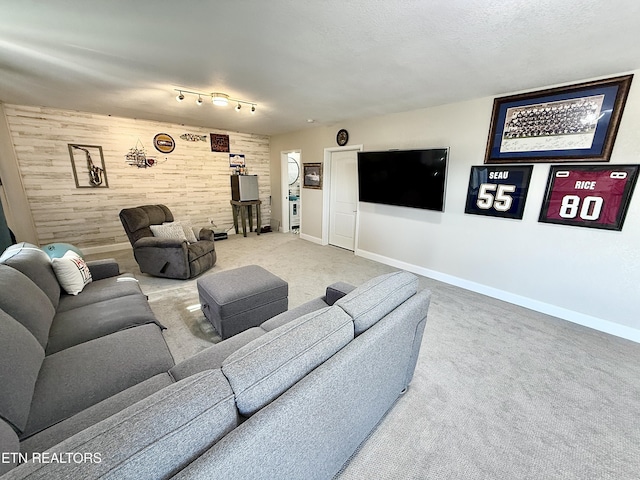 carpeted living room featuring a textured ceiling, wooden walls, an accent wall, baseboards, and rail lighting