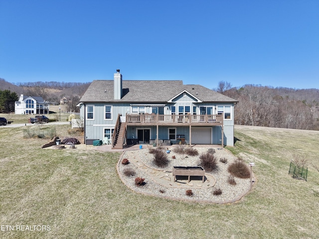 rear view of house with a chimney, a lawn, an attached garage, a deck, and stairs