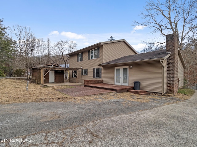 rear view of property featuring french doors, a chimney, and a wooden deck