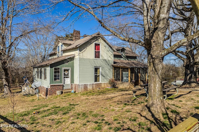 view of side of home with brick siding, a chimney, a lawn, a sunroom, and fence