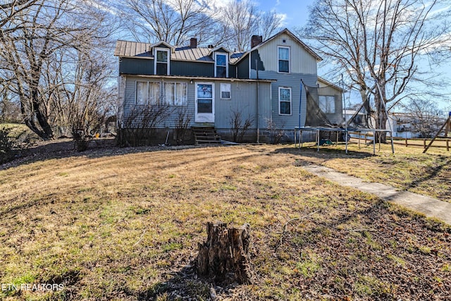 rear view of property with entry steps, a chimney, metal roof, a trampoline, and a yard