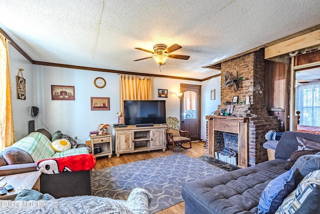 living area with a fireplace, wood finished floors, a ceiling fan, and crown molding