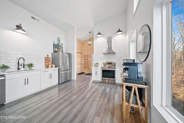 kitchen with stainless steel appliances, a sink, visible vents, white cabinetry, and wall chimney range hood