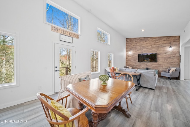 dining area featuring baseboards, a towering ceiling, an accent wall, light wood-style floors, and recessed lighting