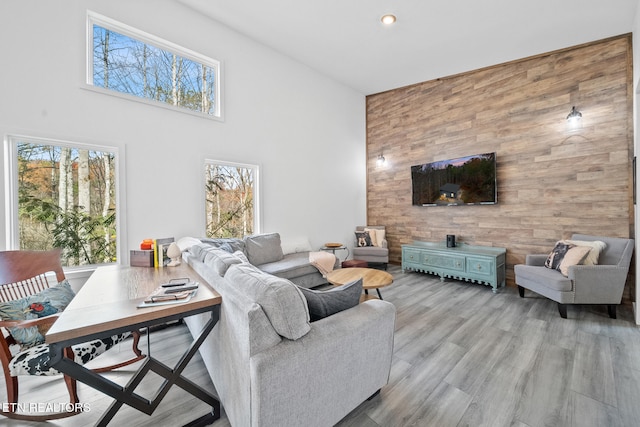 living area with wooden walls, an accent wall, wood finished floors, a high ceiling, and recessed lighting