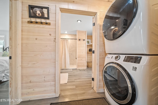 laundry room with stacked washer and dryer, wooden walls, laundry area, and wood finished floors