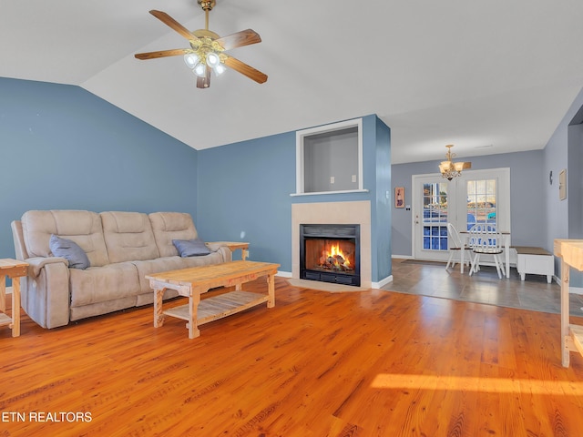 living room with a fireplace with flush hearth, vaulted ceiling, wood finished floors, baseboards, and ceiling fan with notable chandelier