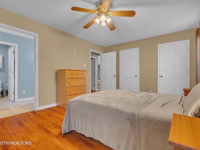 bedroom with light wood finished floors, a ceiling fan, baseboards, and connected bathroom