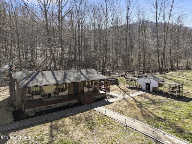 view of front facade featuring an outbuilding, a forest view, a porch, and a shingled roof