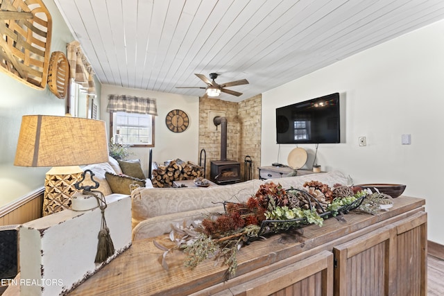 living room with wooden ceiling, wood finished floors, a wood stove, and a ceiling fan