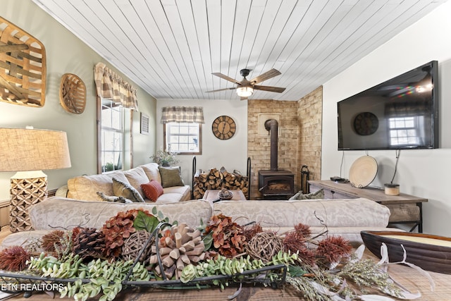 living area featuring wood ceiling, a wealth of natural light, a wood stove, and a ceiling fan