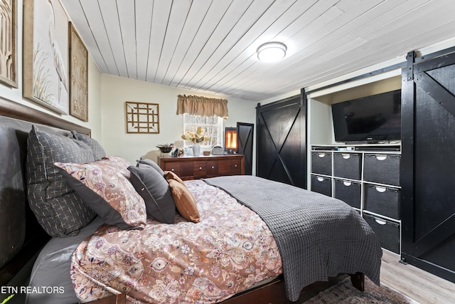 bedroom featuring light wood-type flooring, wood ceiling, and a barn door