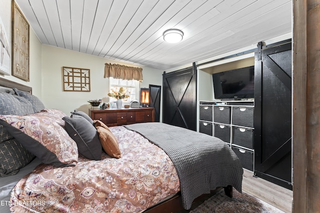 bedroom featuring a barn door, wood ceiling, and light wood-style floors