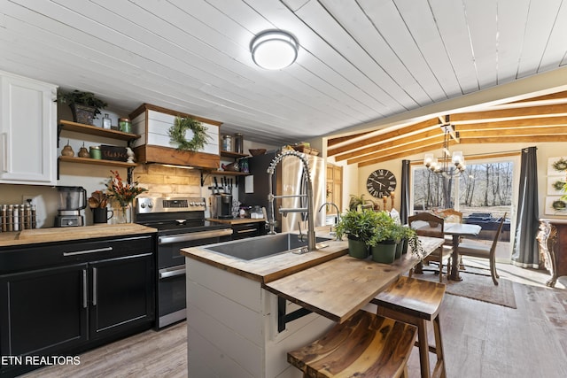 kitchen featuring range with two ovens, butcher block countertops, dark cabinetry, open shelves, and a sink