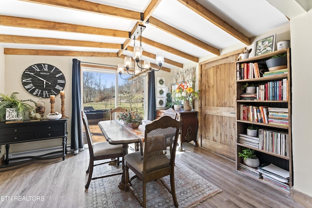 dining area featuring lofted ceiling with beams, a chandelier, and wood finished floors