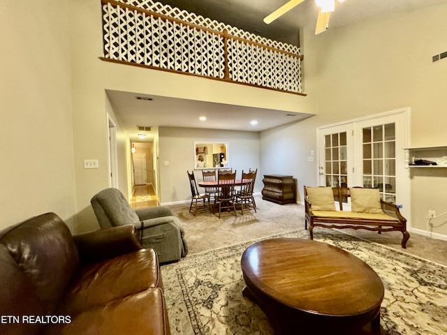 carpeted living area with a ceiling fan, visible vents, a towering ceiling, and baseboards