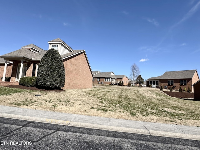 view of side of property with a residential view, brick siding, and a lawn