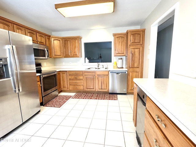 kitchen with light countertops, appliances with stainless steel finishes, brown cabinetry, light tile patterned flooring, and a sink