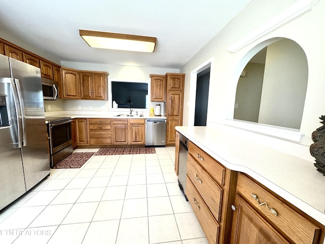 kitchen featuring light tile patterned floors, brown cabinetry, stainless steel appliances, light countertops, and a sink