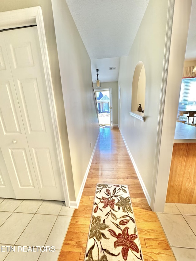 corridor featuring a textured ceiling, light wood-type flooring, visible vents, and baseboards