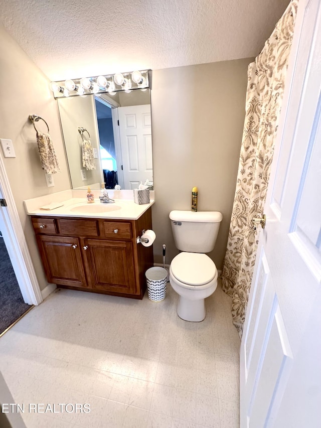 bathroom with baseboards, vanity, toilet, and a textured ceiling