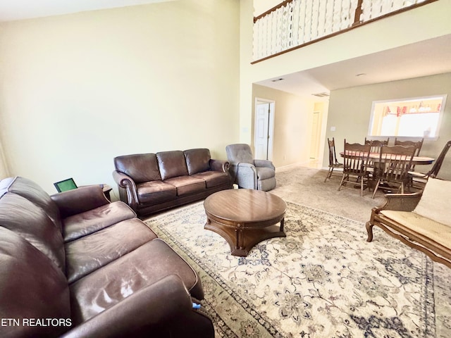 living area featuring a towering ceiling, baseboards, and carpet flooring