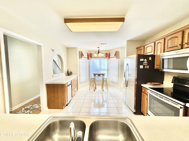 kitchen featuring light tile patterned floors, a chandelier, light countertops, appliances with stainless steel finishes, and brown cabinets