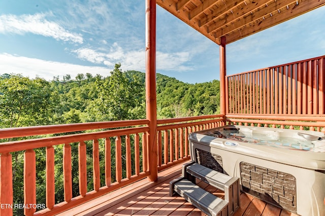 wooden deck with a view of trees and a hot tub