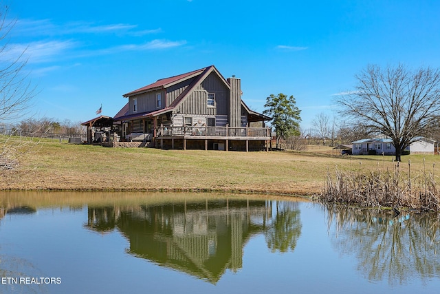 back of house featuring a chimney, a lawn, and a water view