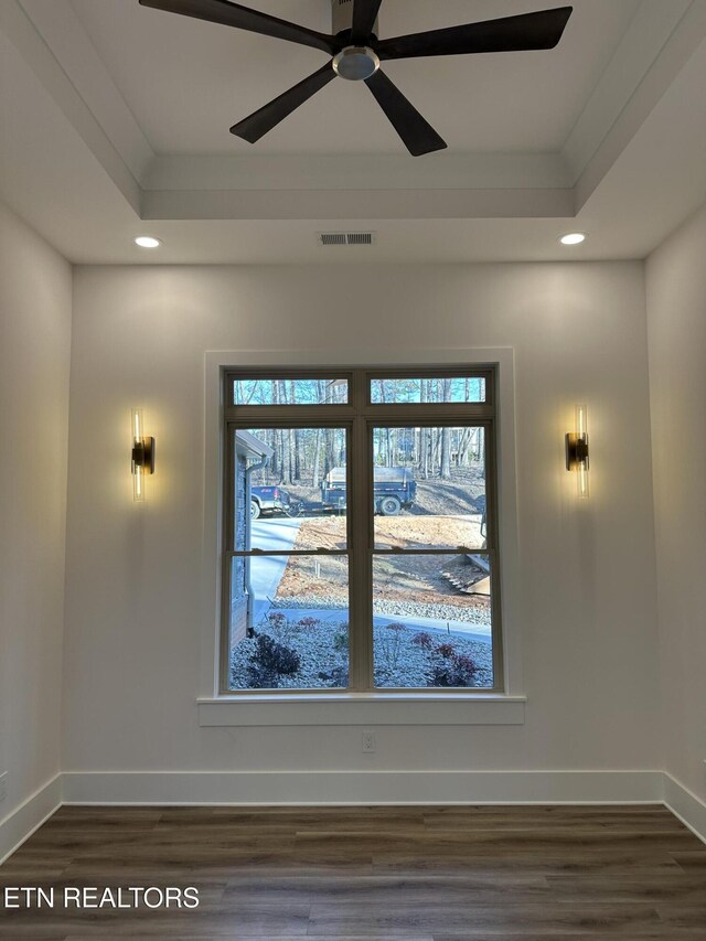 interior space featuring a tray ceiling, visible vents, baseboards, and wood finished floors