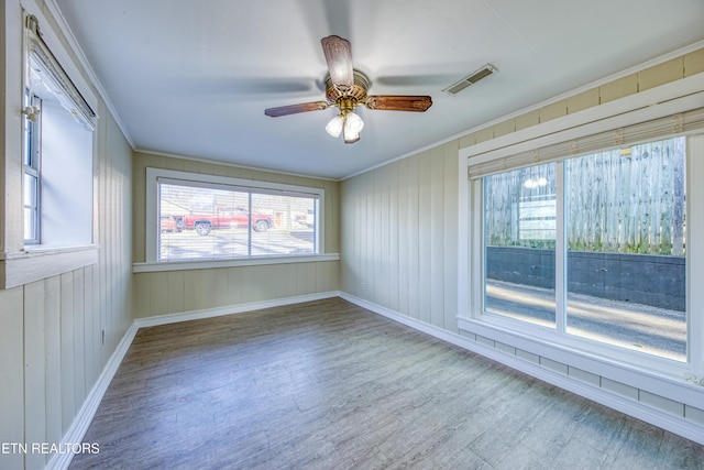 spare room featuring ceiling fan, wood finished floors, visible vents, baseboards, and crown molding