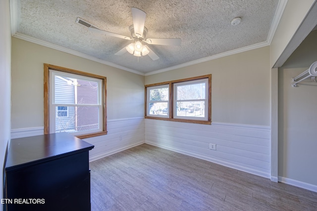 unfurnished bedroom featuring a textured ceiling, ceiling fan, wood finished floors, wainscoting, and crown molding