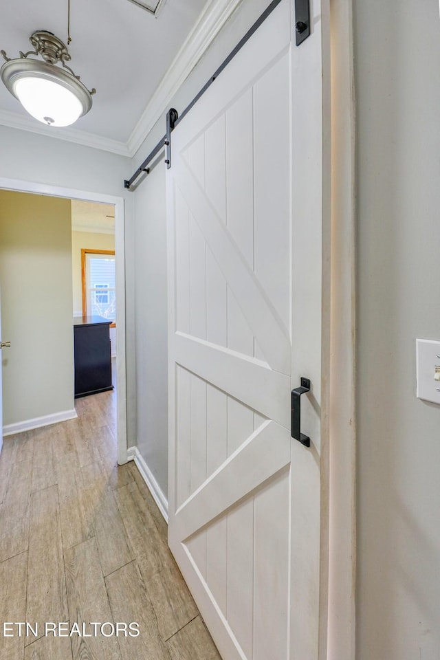 corridor featuring ornamental molding, light wood-style flooring, baseboards, and a barn door