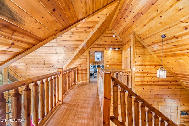 hallway with vaulted ceiling, light wood-type flooring, an upstairs landing, and wooden walls