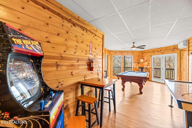 rec room featuring a paneled ceiling, an AC wall unit, wooden walls, wood finished floors, and billiards