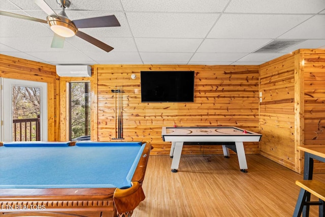 rec room featuring a drop ceiling, a ceiling fan, wood walls, wood finished floors, and a wall mounted air conditioner