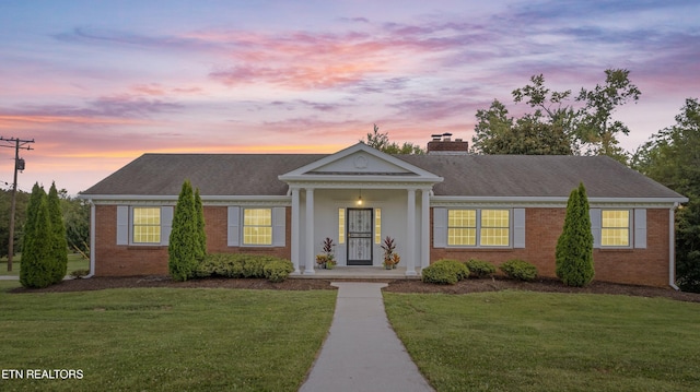 view of front of property with brick siding, a lawn, and a chimney