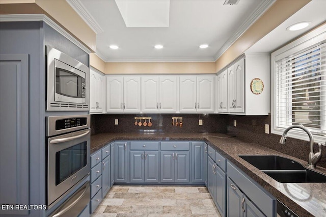 kitchen with a sink, white cabinetry, ornamental molding, appliances with stainless steel finishes, and a warming drawer