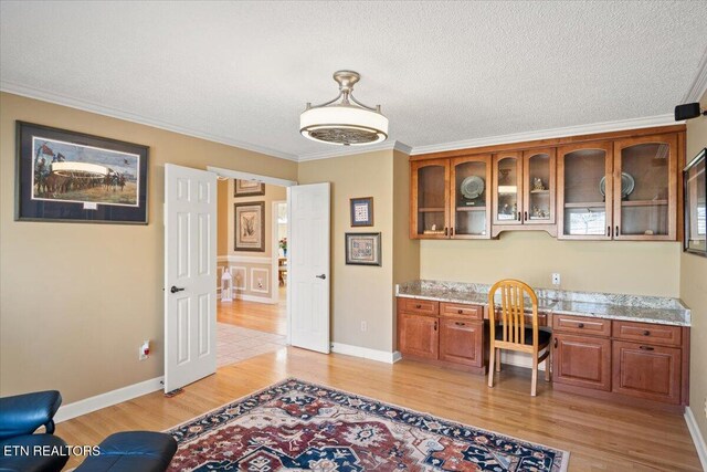 office area with light wood finished floors, built in desk, a textured ceiling, and ornamental molding