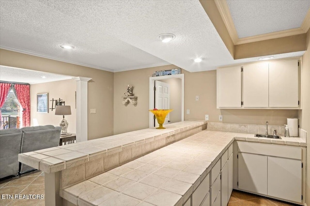 kitchen with tile countertops, a peninsula, ornamental molding, and open floor plan