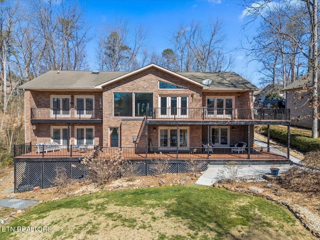 back of house with french doors, brick siding, a lawn, and a balcony