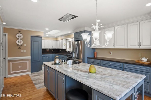 kitchen with a skylight, visible vents, light wood-style floors, white cabinets, and stainless steel fridge