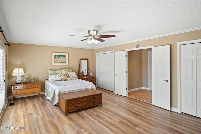 bedroom featuring ornamental molding, light wood-style floors, a textured ceiling, and multiple closets