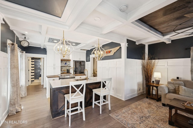 interior space with dark wood finished floors, a decorative wall, an inviting chandelier, coffered ceiling, and beamed ceiling