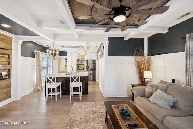 living area with light wood finished floors, visible vents, a decorative wall, coffered ceiling, and beamed ceiling