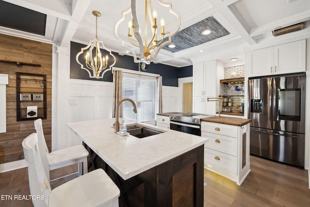 kitchen with butcher block countertops, a center island with sink, stainless steel appliances, a sink, and a chandelier